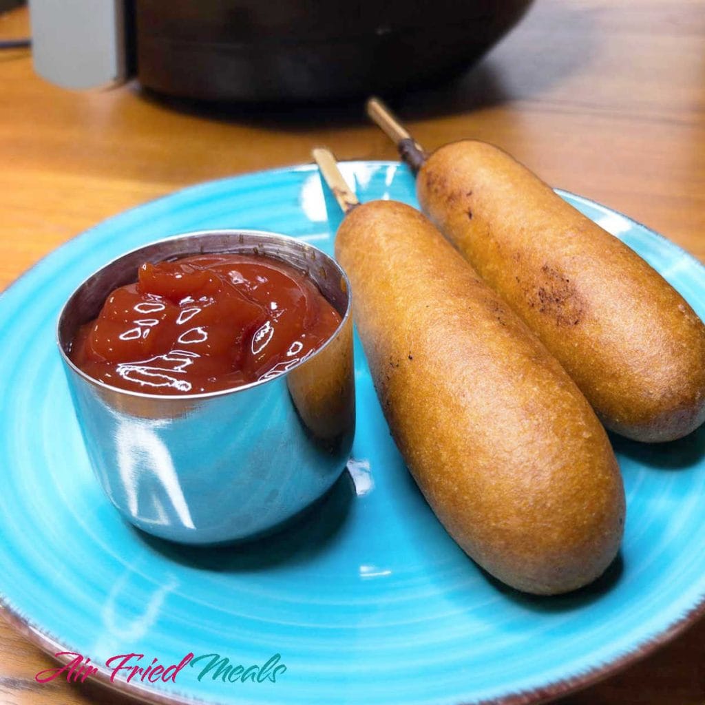 two corn dogs on a blue plate with a metal container with ketchup.