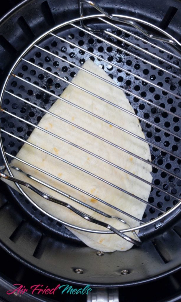 Tortilla in air fryer basket with air fryer rack on edge.