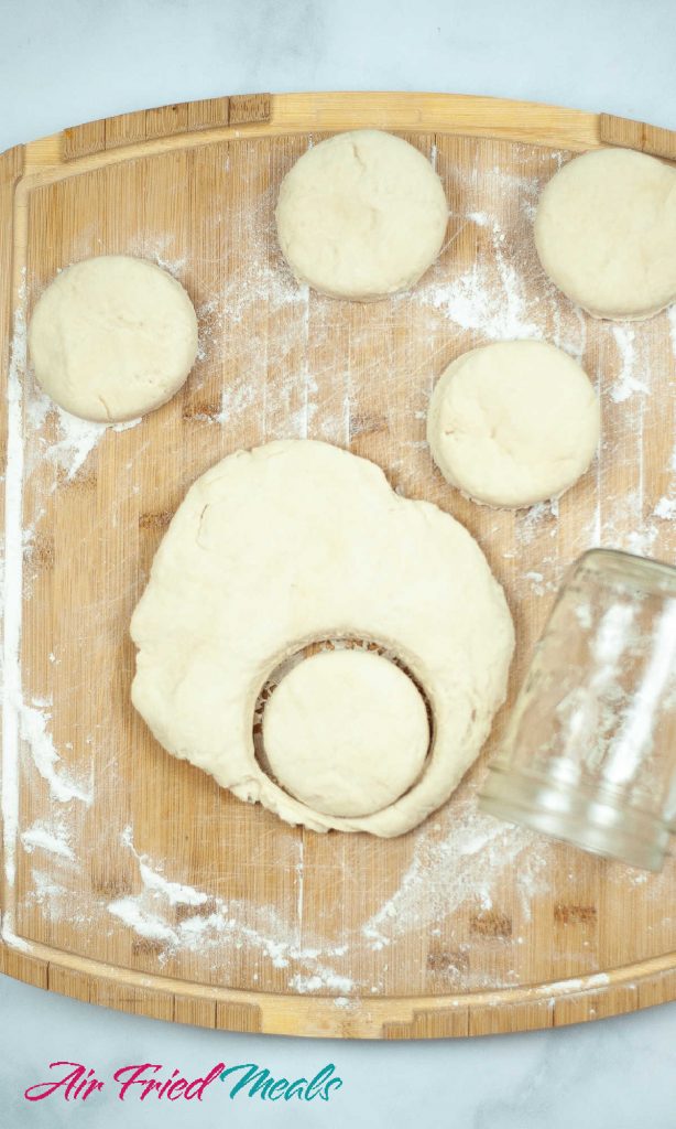4 cut out biscuits on top, dough with a cut out biscuit still in it and a mason jar to the side.
