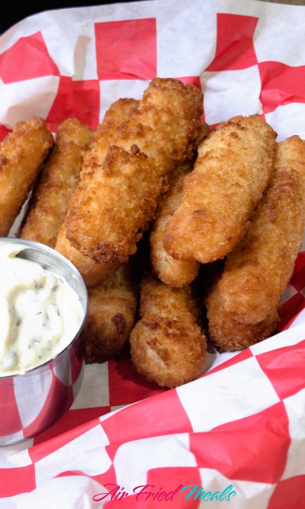 closeup of fish sticks in a pile with a container of tartar sauce next to it.