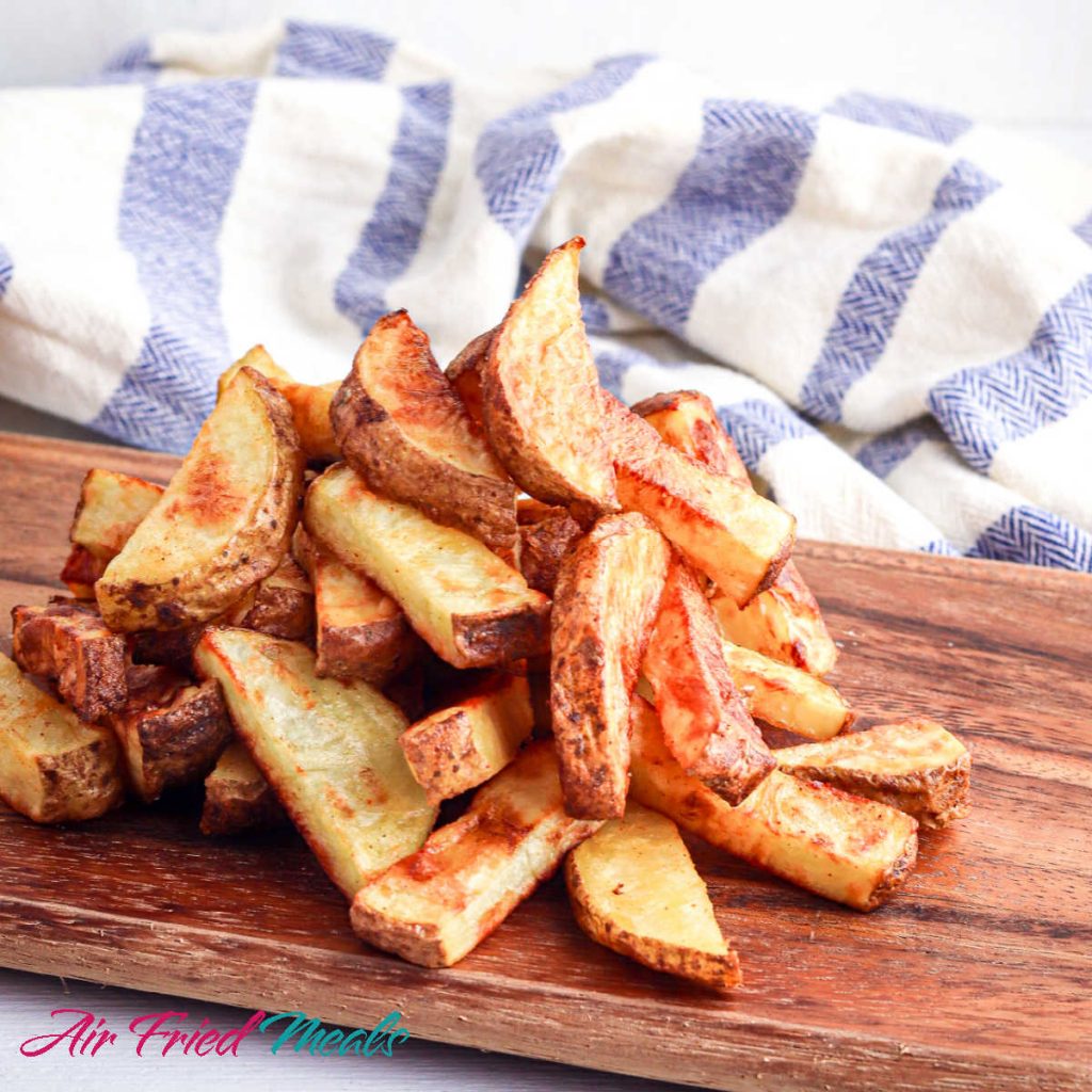 cooked air fryer potato wedges on a cutting board with a blue and white towel behind.