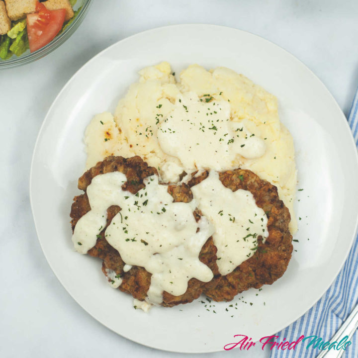 Top down view of chicken fried steak with gravy and mashed potatoes on a plate.