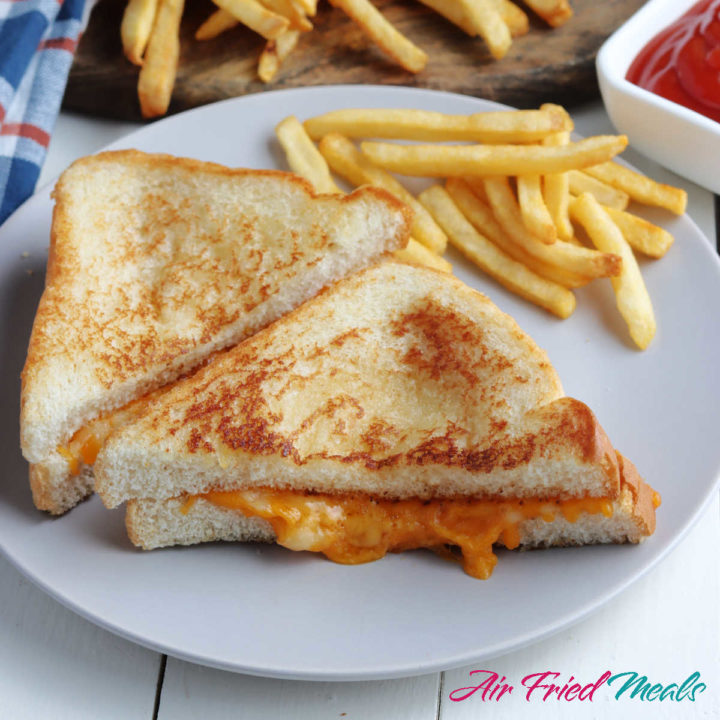 Two halves of a grilled cheese sandwich on a white plate with fries.