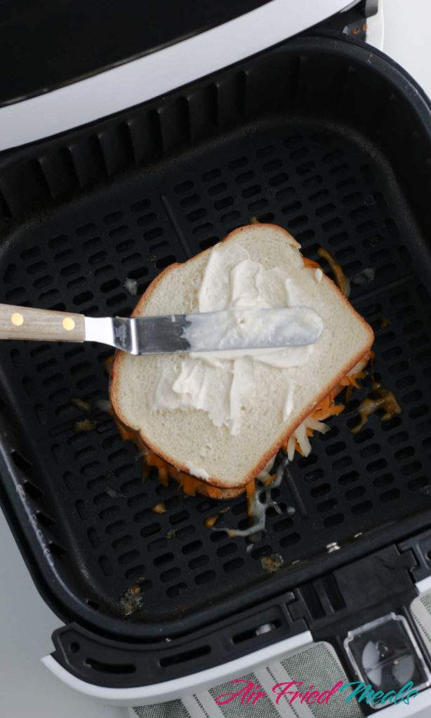 Compiled cheese sandwich in air fryer with mayo being spread across top slice of bread.