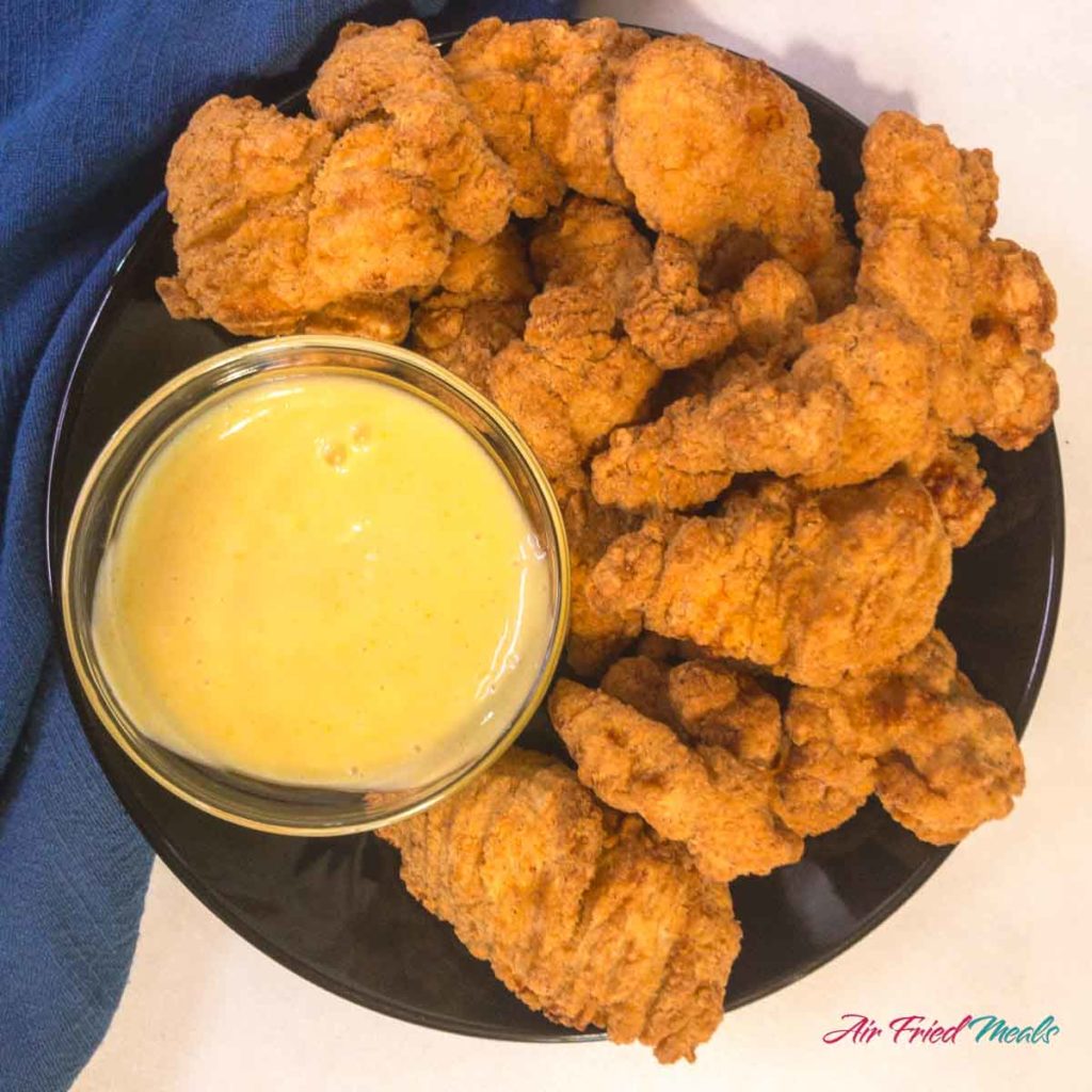 top down view of popcorn chicken on a plate with a small bowl of honey mustard dipping sauce.