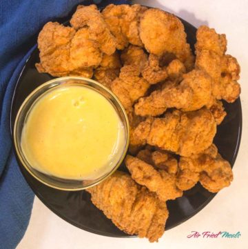 top down view of popcorn chicken on a plate with a small bowl of honey mustard sauce.