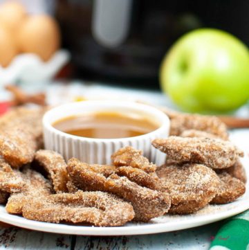 Air Fryer Apple Fries around a container of caramel sauce on a plate.