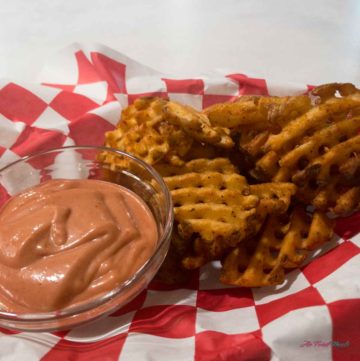 basket of waffle fries with a small dish of dipping sauce.