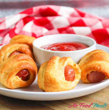 Pigs in a blanket with a bowl of ketchup behind.