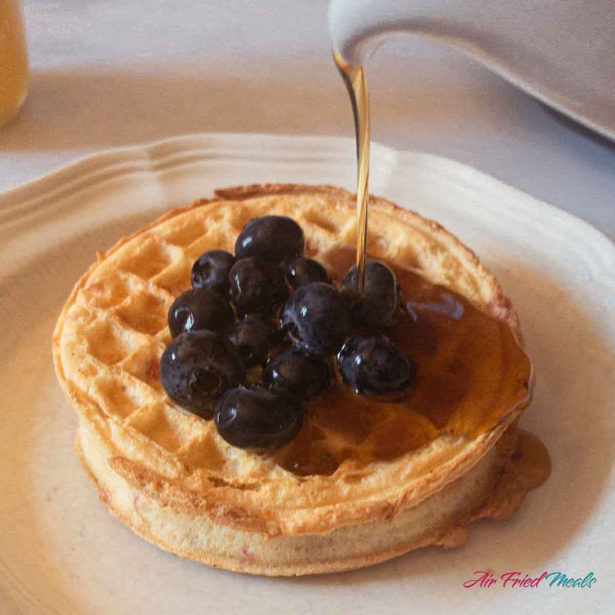 Syrup being poured on waffles with blueberries on top.