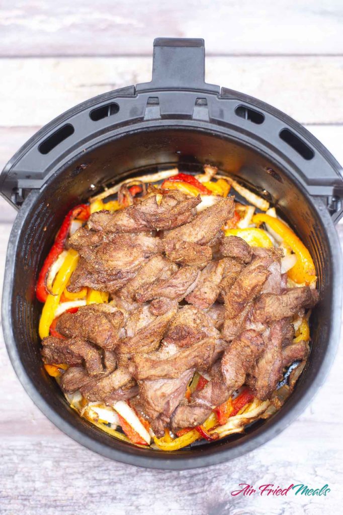 Top down view of cooked vegetables with steak on top in an air fryer basket.