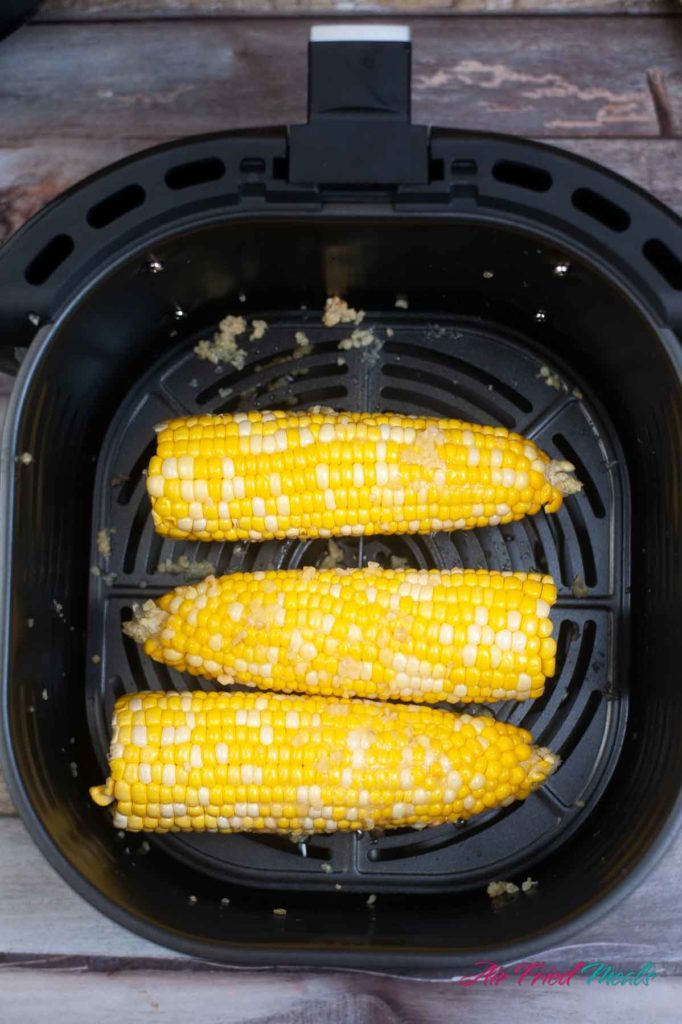 Raw corn on the cob in an air fryer basket.